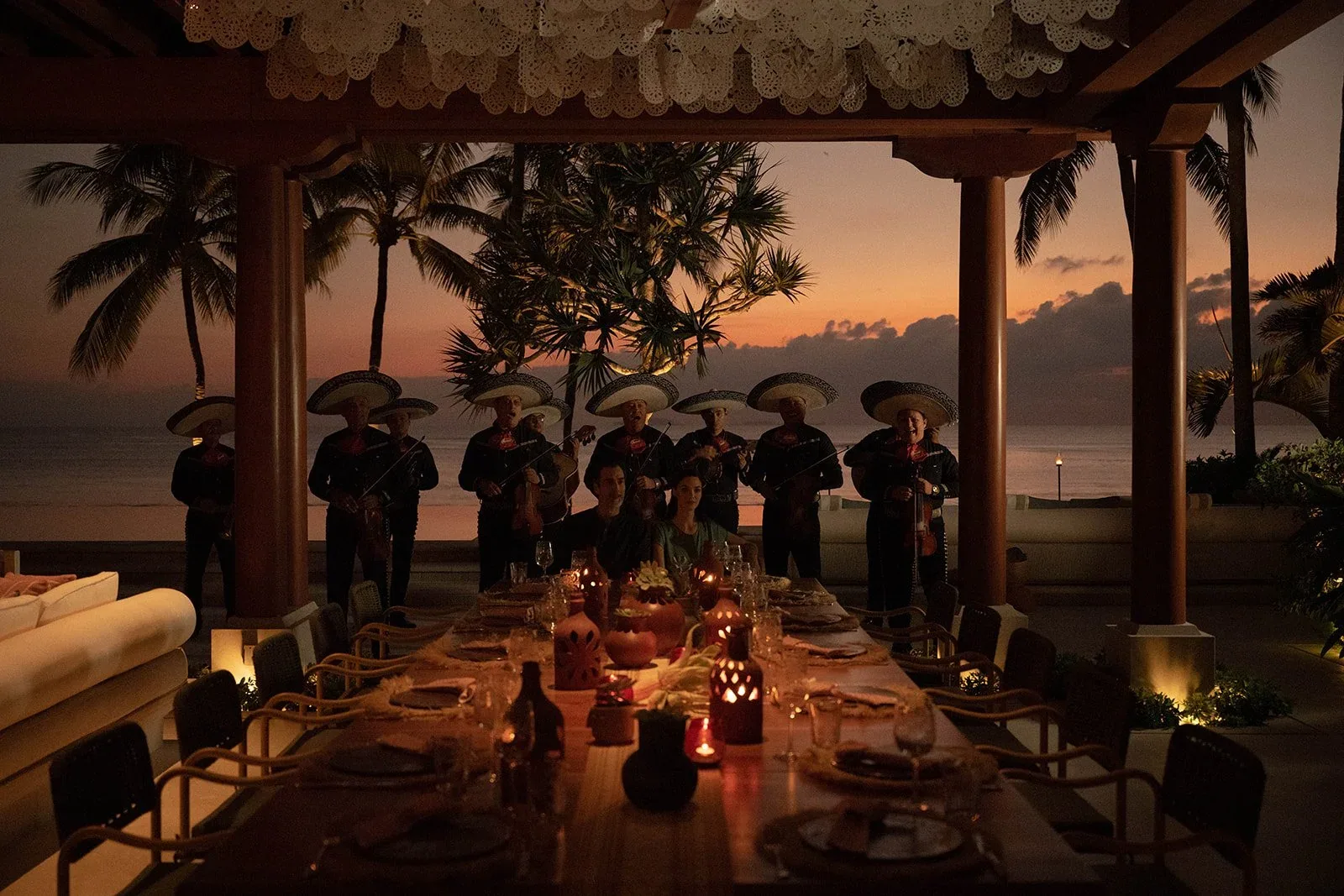 A long candlelit dinner table under the pavilion with mariachi musicians playing