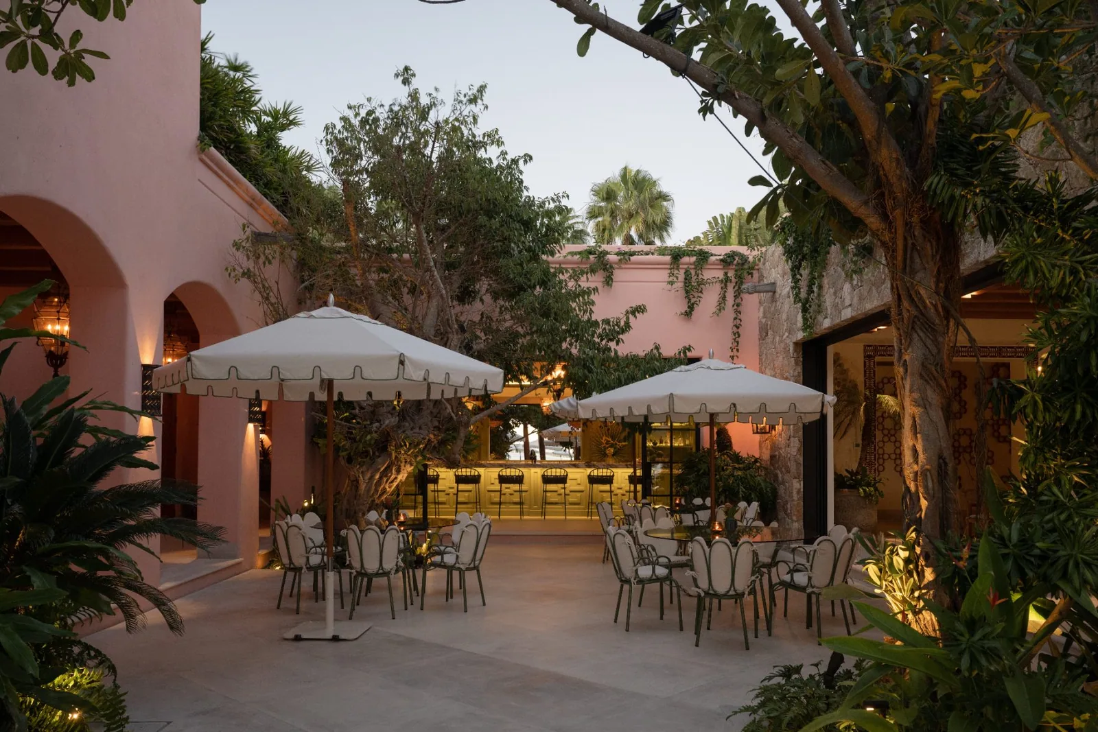 The courtyard caf&eacute; under white umbrellas, framed by pink hacienda walls and palms
