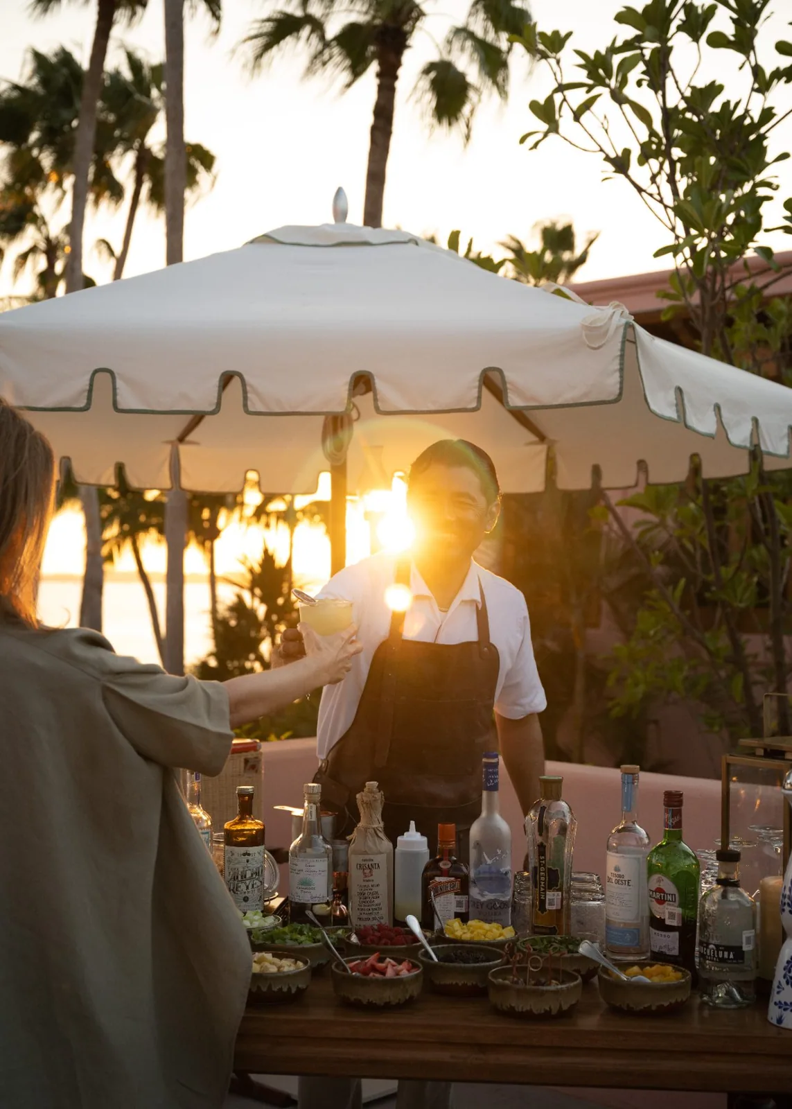 A bartender mixing sundowners beneath a parasol at golden hour