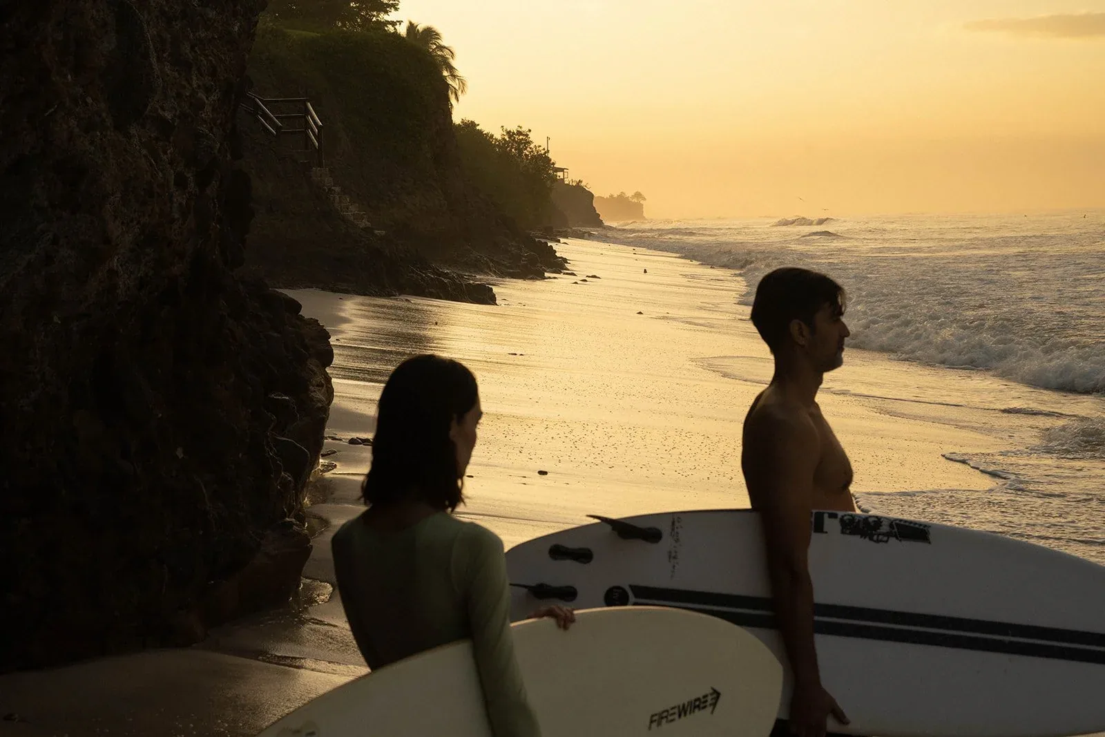 Two surfers carrying their boards along the beach at dusk