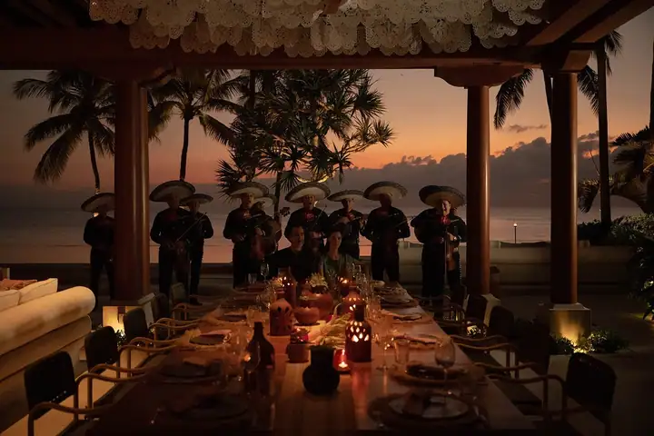A long candlelit dinner table under the pavilion with mariachi musicians playing