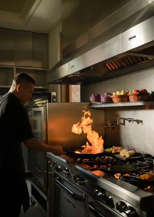 A chef working over open flame at the range in the commercial kitchen