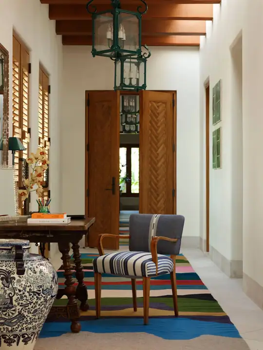 A long hacienda hall with a striped rug, carved chairs and a lantern