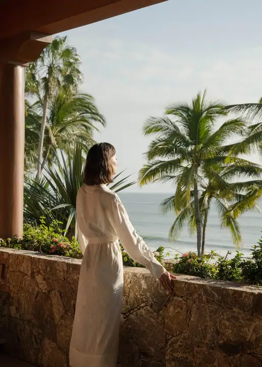 A guest in a robe on a stone terrace, looking out to the Pacific in the morning