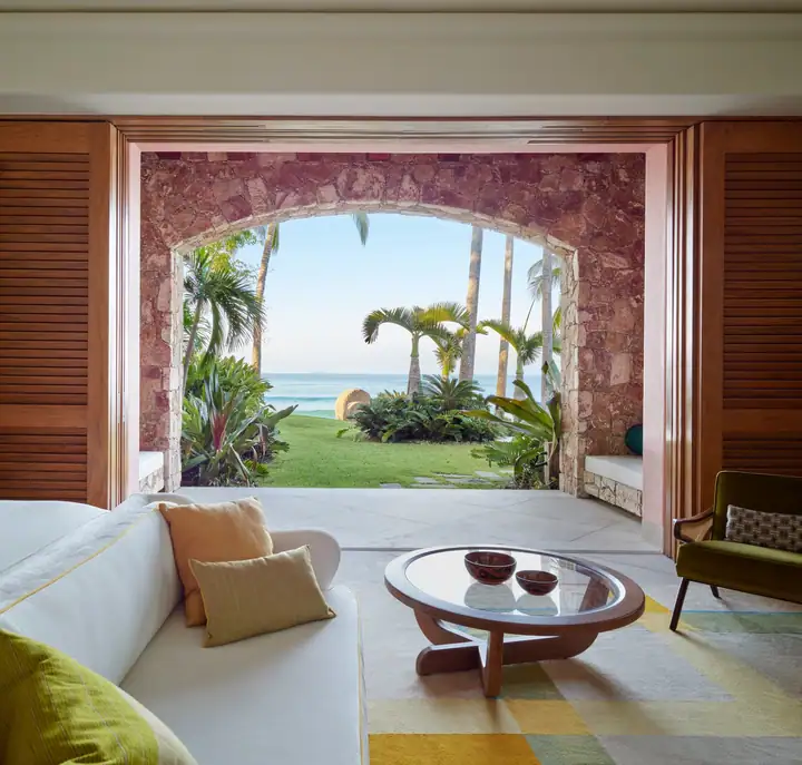 A ground-floor oceanfront suite&rsquo;s living area, arched open to the palms and the sea