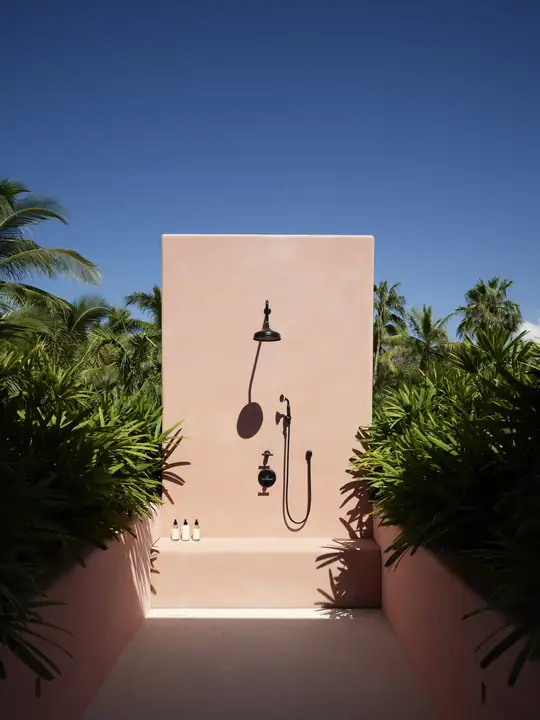 An outdoor shower terrace against a pink plastered wall, planted on both sides
