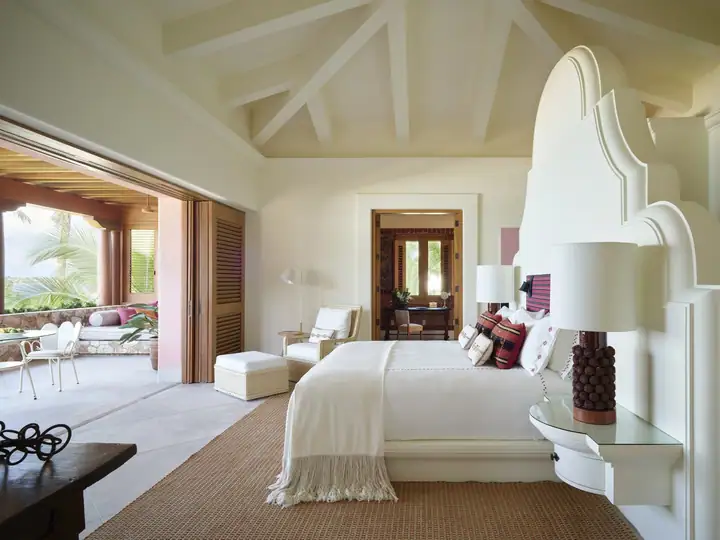 A principal suite with a tall scalloped headboard, opening to the pool terrace