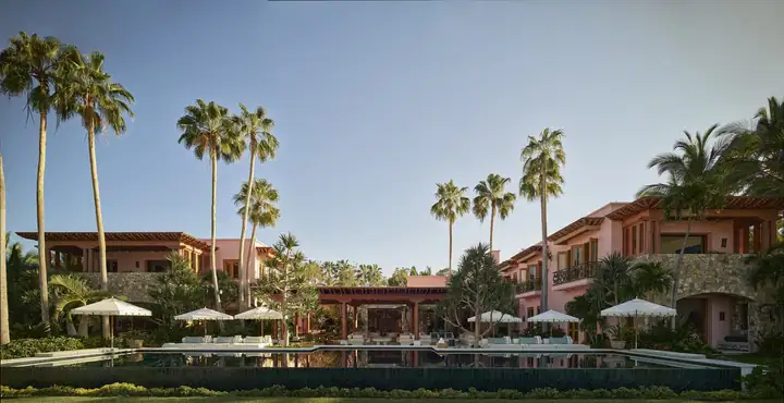 The pink hacienda ranges of the estate behind their coconut palms, pool and lawn in evening light