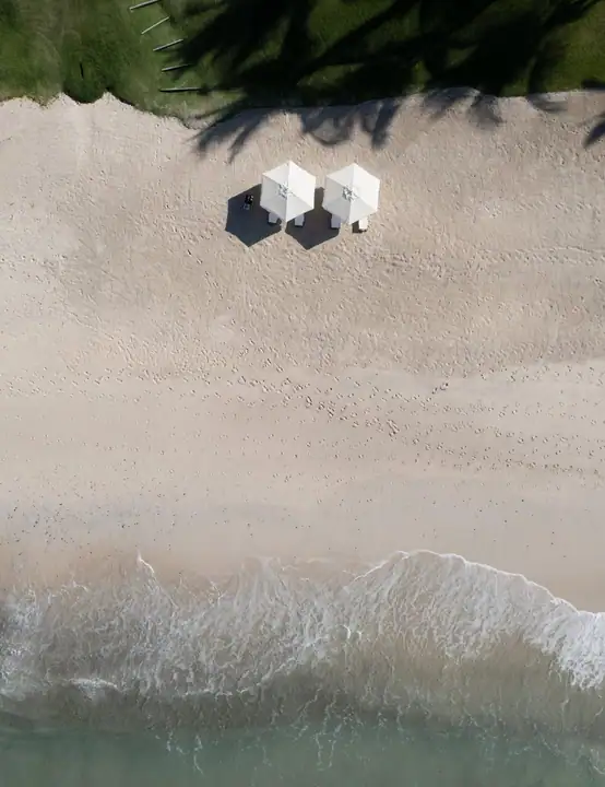 Two white umbrellas on the estate&rsquo;s white-sand cove, seen from above