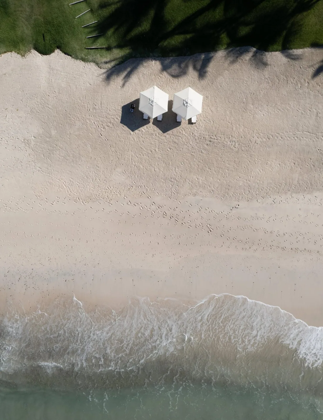 Two white umbrellas on the estate&rsquo;s white-sand cove, seen from above
