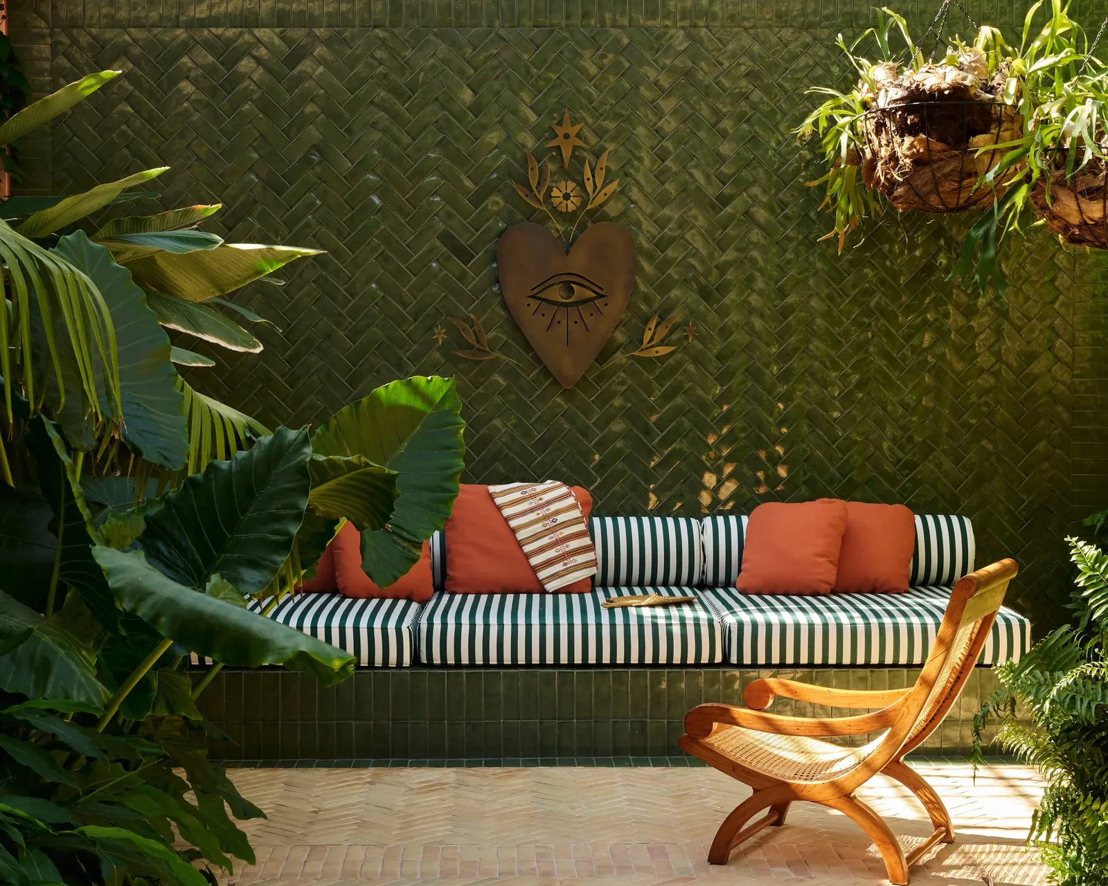 A striped sofa and folding chair against a woven green wall hung with plants